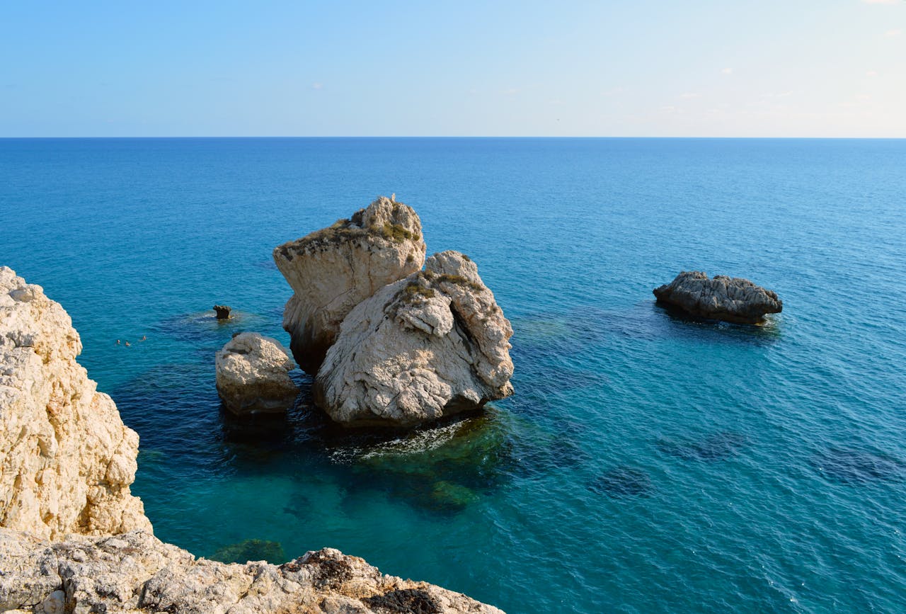 services-02 Beautiful view of Aphrodite's Rock in Cyprus, showcasing the serene blue ocean and rugged formations.