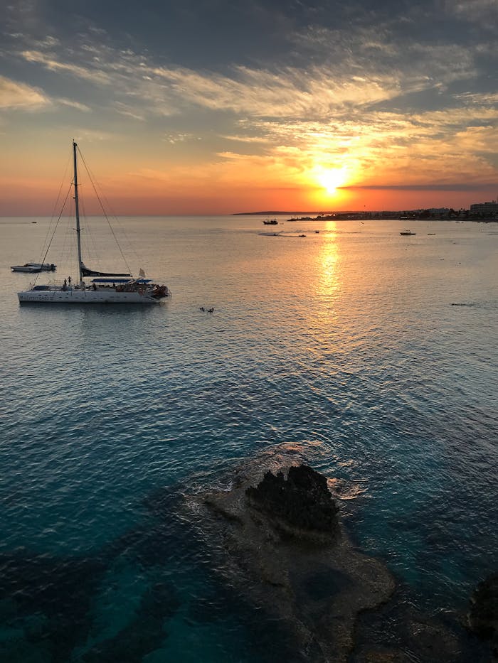A serene sunset over a sailboat in Ayia Napa, Cyprus, capturing vibrant colors and calm seas.