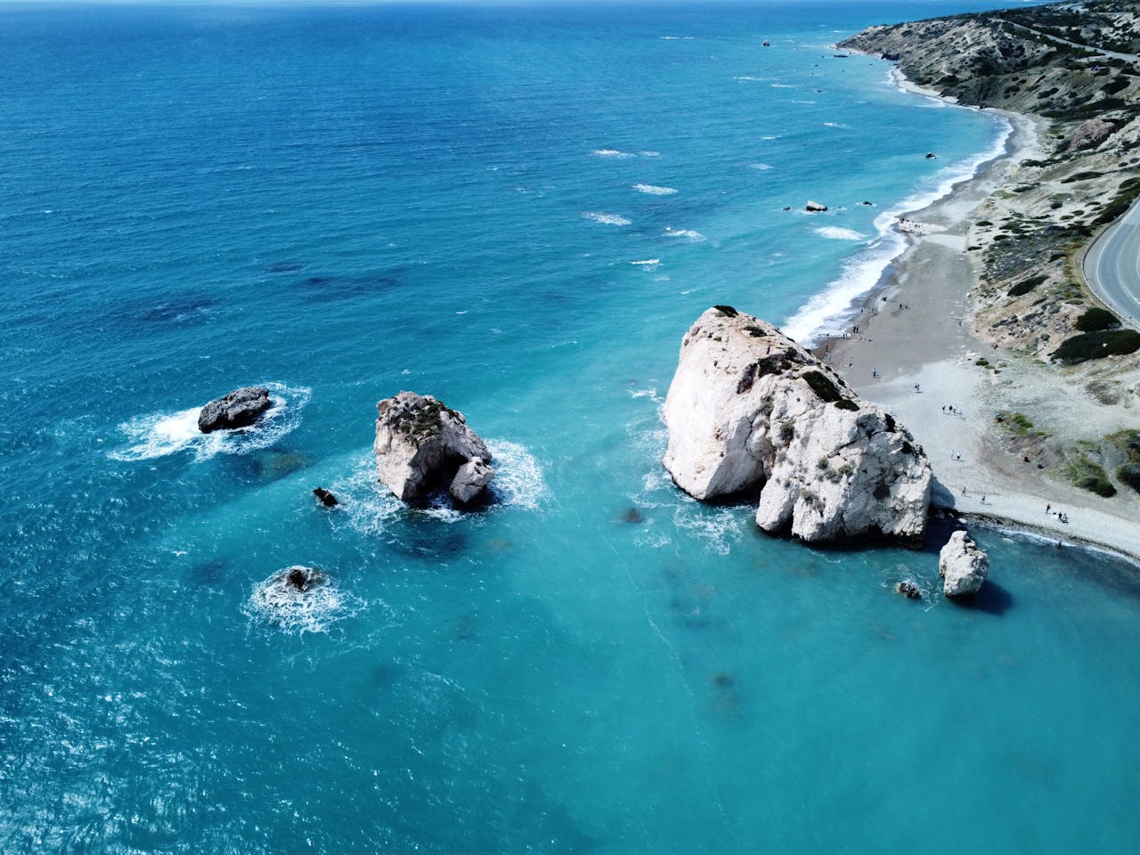 services-04 Stunning aerial view of Aphrodite's Rock, a famous coastal formation in Cyprus, in vibrant blue waters.