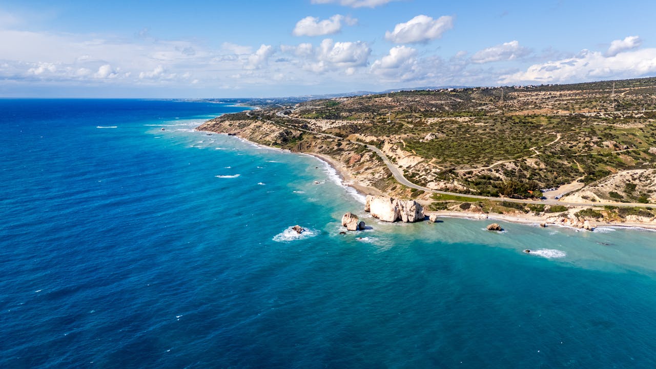 Stunning aerial photograph of Aphrodite's Rock on Cyprus coastline, surrounded by vibrant blue waters.